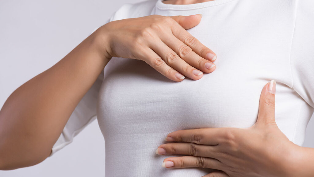 Close up shot of a woman in a white shirt giving herself a breast exam